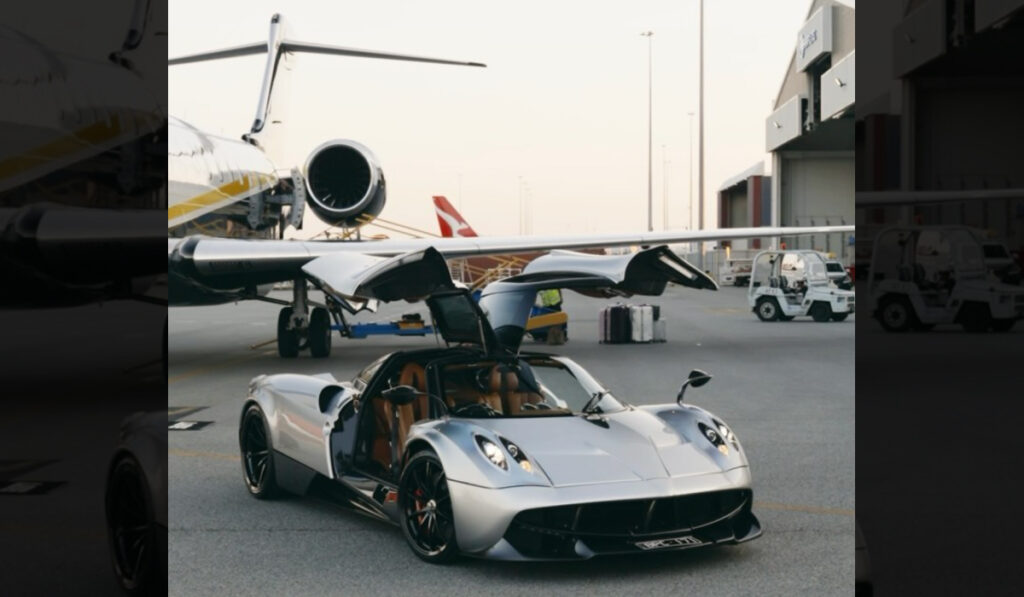 Hopeanvärinen Pagani Huayra -urheiluauto, jonka ovet ovat auki, seisoo yksityiskoneen edessä lentokentällä auringonlaskun aikaan.