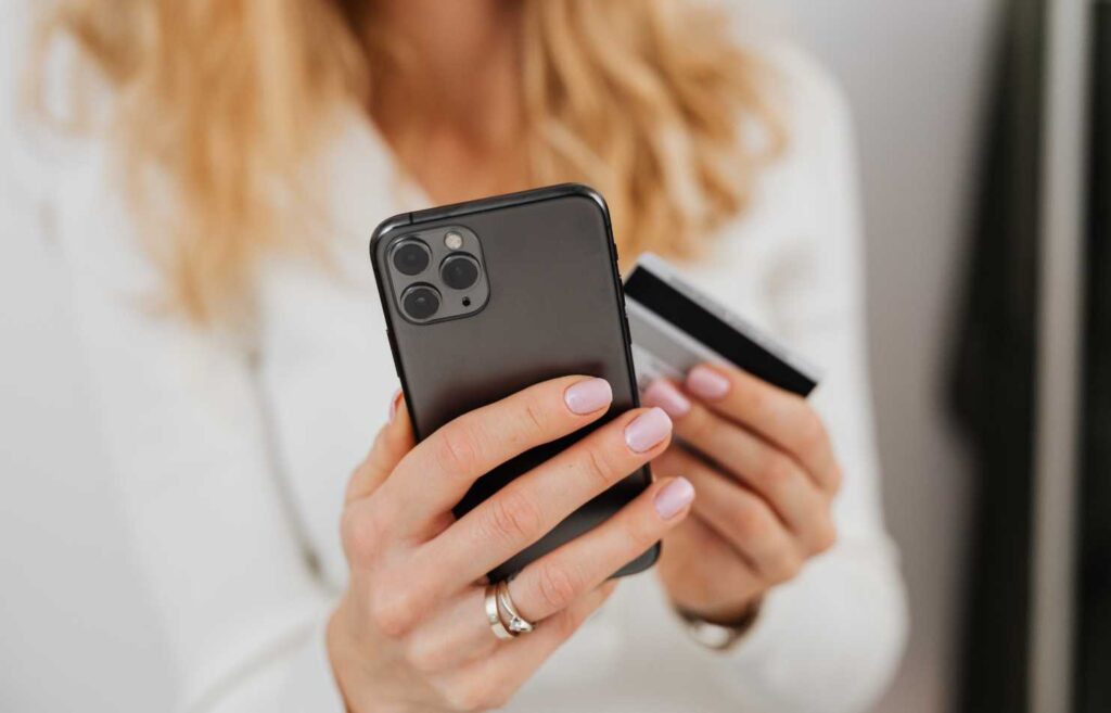 Kuvassa naisella on kädessä mobiililaite ja pankkikortti