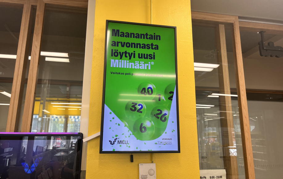 Kuvassa Helsingin Rautatieaseman R-kioskin kyltti kertoo Millin tulosten sisältäneen päävoiton 12.8. Hieman pienemmällä lukee että voittanut kuponki pelattiin Pielavedellä.