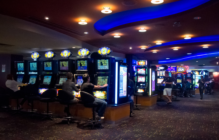 Asiakkaita pelaamassa rahapeliautomaateilla hämärästi valaistussa pelisalissa