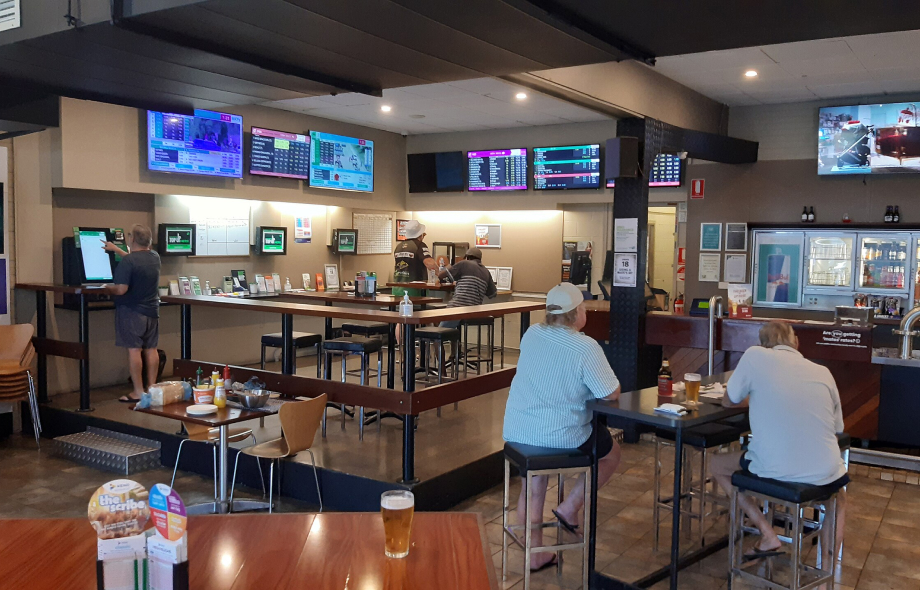 Miehiä urheiluvedonlyöntibaarissa seuraamassa kisoja ja käyttämässä vedonlyöntipäätteitä Australiassa

