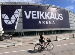 Kuvassa Veikkaus Arena Helsingissä. Veikkauksen mainoskylttiä vielä asennetaan. Etualalla pyöräilijä.
