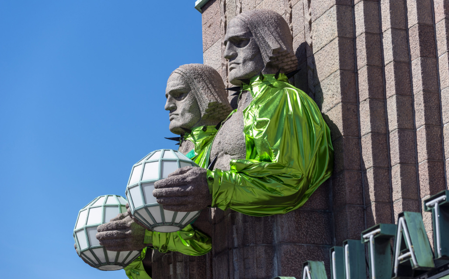 Käärijän boleroasuihin puetut Lyhdynkantaja-patsaat Helsingin rautatieasemalla kirkkaana kevätpäivänä.