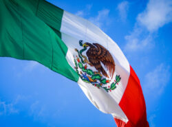Meksikon lippu liehuu sinistä taivasta vasten.