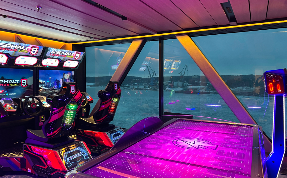 Paf pelihuone laivalla. Kuvassa näkyy esimerkiksi ilmakiekko ja rallipeli. Taustalla tummanpuhuva satamamaisema.