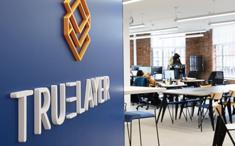 Oranssi-valkoinen Truelayer logo toimiston taivaan sinisellä seinällä