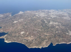 Maltan saari lentokoneesta kuvattuna. Pääkaupunki Valletta ja Grand Harbor näkyvät yläkulmassa. Kallioista etelärannikkoa etualalla.