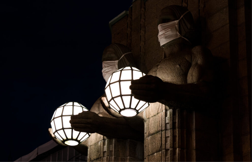 Helsingin Rautatieaseman Lyhdynkantajat käyttävät kasvosuojia koronapandemian aikana iltahämärässä.