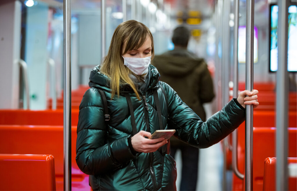 Kasvomaskia käyttävä nainen seisoo pääkaupunkiseudun metrossa ja katsoo puhelintaan korona-aikana.