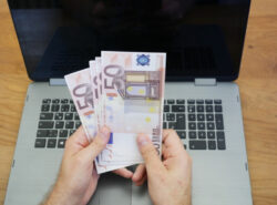 Mies pitää euron seteleitä tietokoneen edessä.