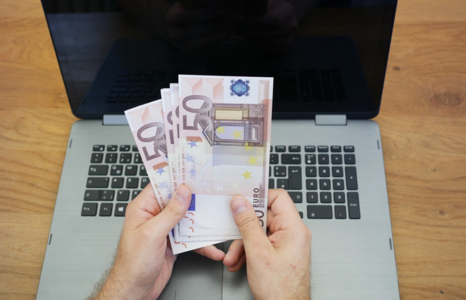 Mies pitää euron seteleitä tietokoneen edessä.