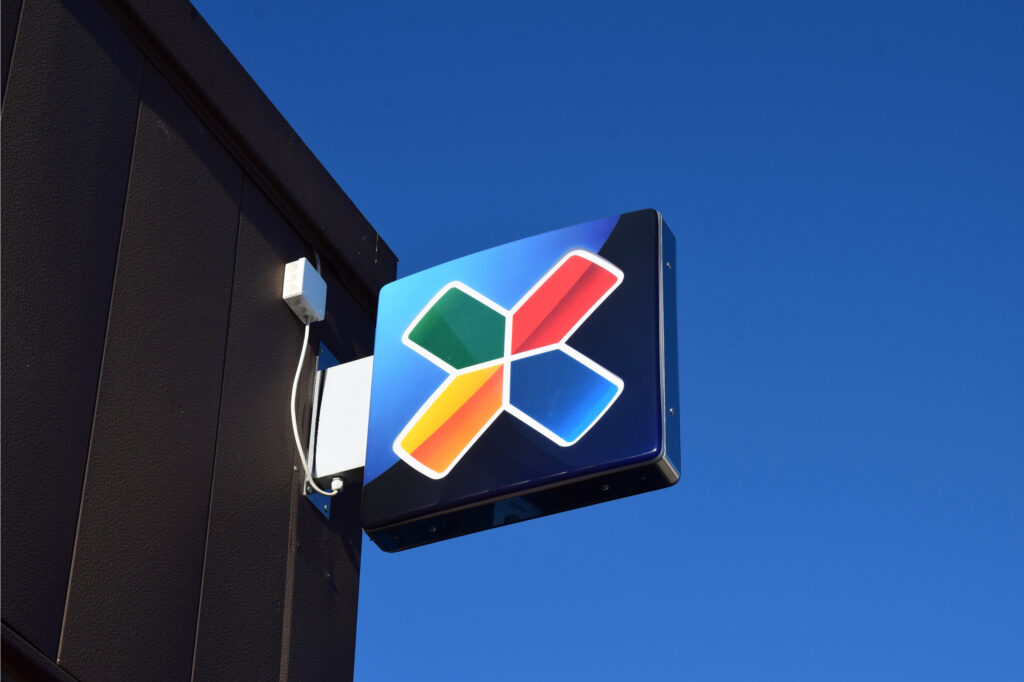 Monivärinen X-logo seinäkyltissä sinistä taivasta vasten.