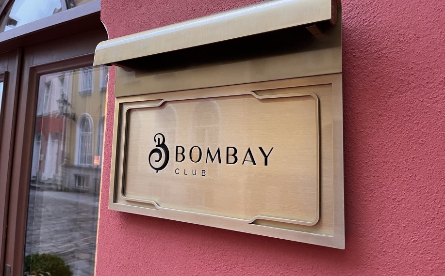 Bombay Club kyltti Tallinan vanhassakaupungissa Rataskaevu kadulla. Kultainen kyltti ja punertava talo. Vieressä näkyy kasinon ovi.
