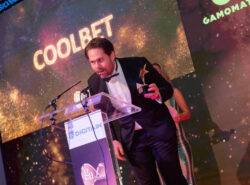 Endre Nesset hyväksymässä palkintoa pitäen puhetta. Taustalla kiiltävä Coolbet logo.