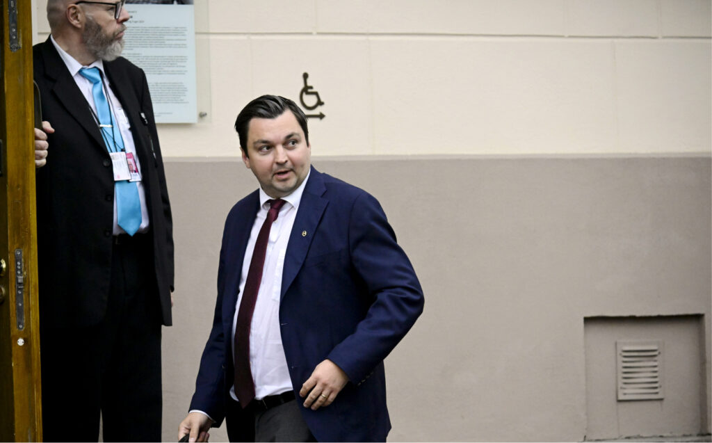 Turvamies pitelee ovea auki Joakim Strandille joka kantaa salkkua. Molemmat puvuissa ja kravaataeissa.