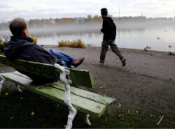 Mies istuu penkillä Töölönlahden rannalla Toinen mies juoksee ohi. Vaatteiden perusteella 2008-2012.