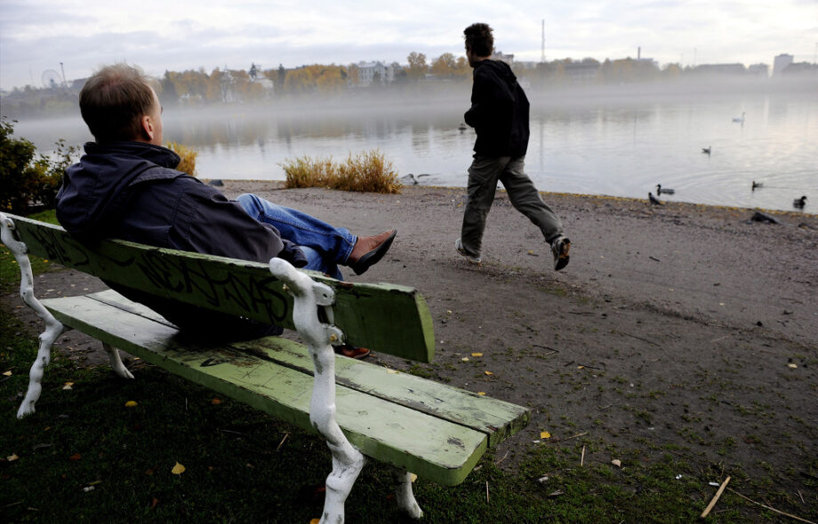 Mies istuu penkillä Töölönlahden rannalla Toinen mies juoksee ohi. Vaatteiden perusteella 2008-2012.