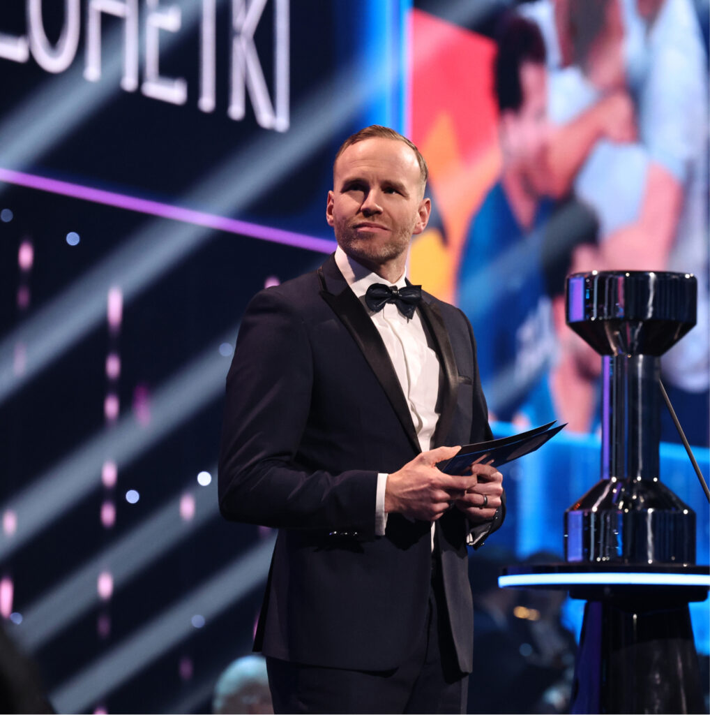 Mika Poutala lavalla pokaalin vieressä Urheilugaalassa 2026, kädessä puhujan muistilappuja.