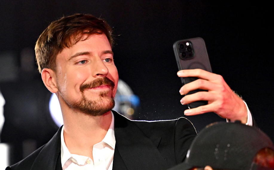 Mr. Beast hymyilee ja pitää puhelinta kädessään.