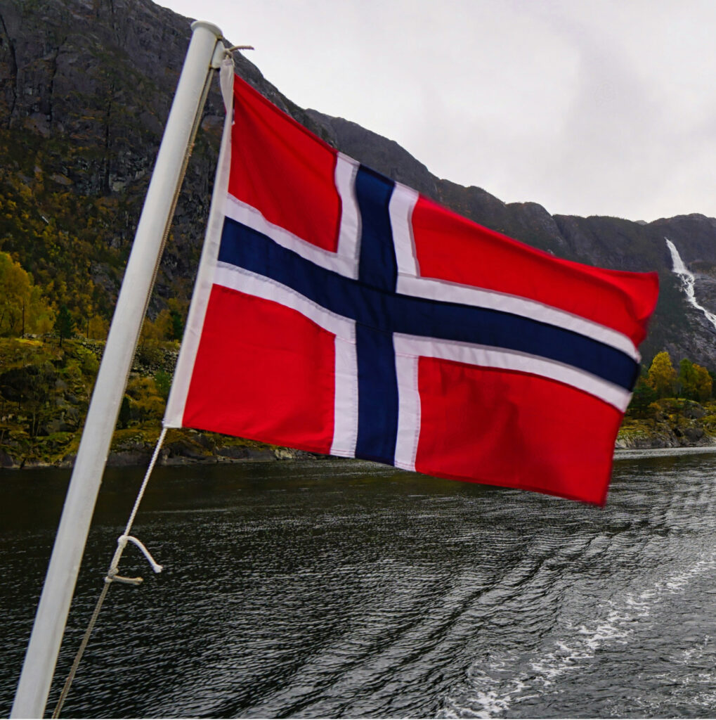 Norjan lippu liehumassa vuonon ja vuoriston edessä Norjassa.