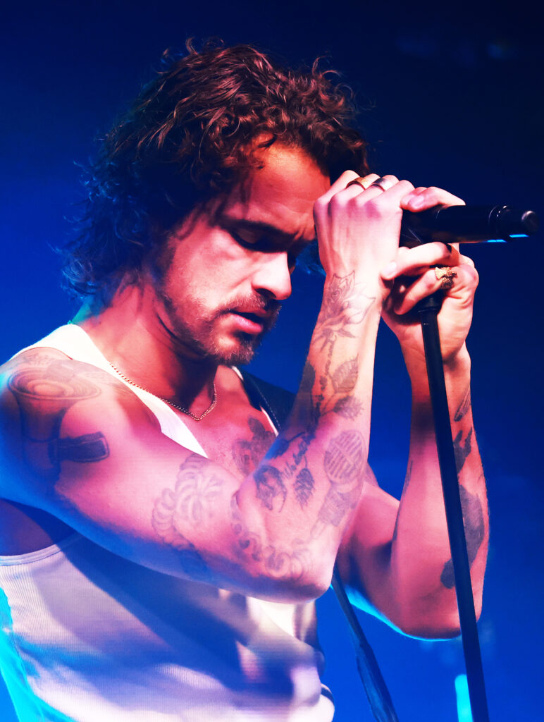 Parkkonen pitelee mikrofonia tunteikkaasti. Tatuoidut kädet. 