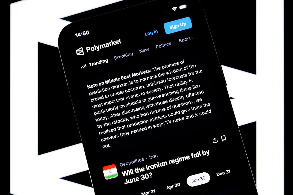 Älypuhelimen näytöllä näkyy Polymarket-sovellus. Näytöllä on huomautus “Note on Middle East Markets”, jossa Polymarket sanoo ennustemarkkinoiden tarjoavan tarkempia ja puolueettomampia vastauksia Lähi-idän hyökkäyksiin liittyviin kysymyksiin kuin tv-uutiset tai X. Sen alla näkyy veto, jossa kysytään kaatuuko Iranin hallinto kesäkuun loppuun mennessä.
