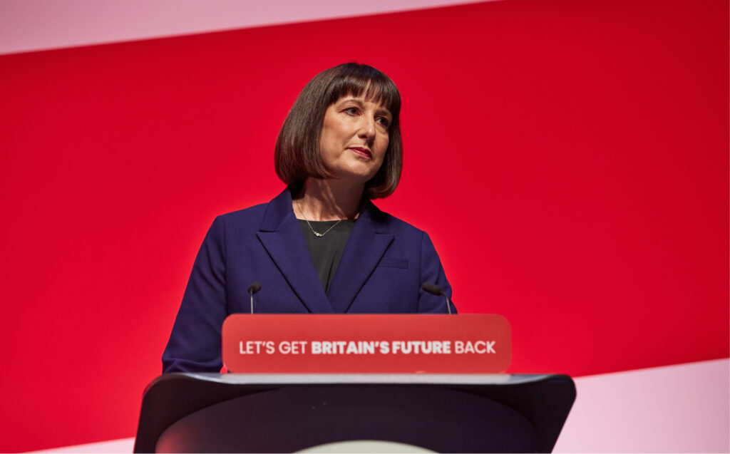 Britannian poliitikko Rachel Reeves puhuu Labour-puolueen puoluekokouksessa puhujakorokkeella Liverpoolissa vuonna 2023. Taustalla punainen lavatausta ja puheenpöntössä Labourin kampanjalause.
