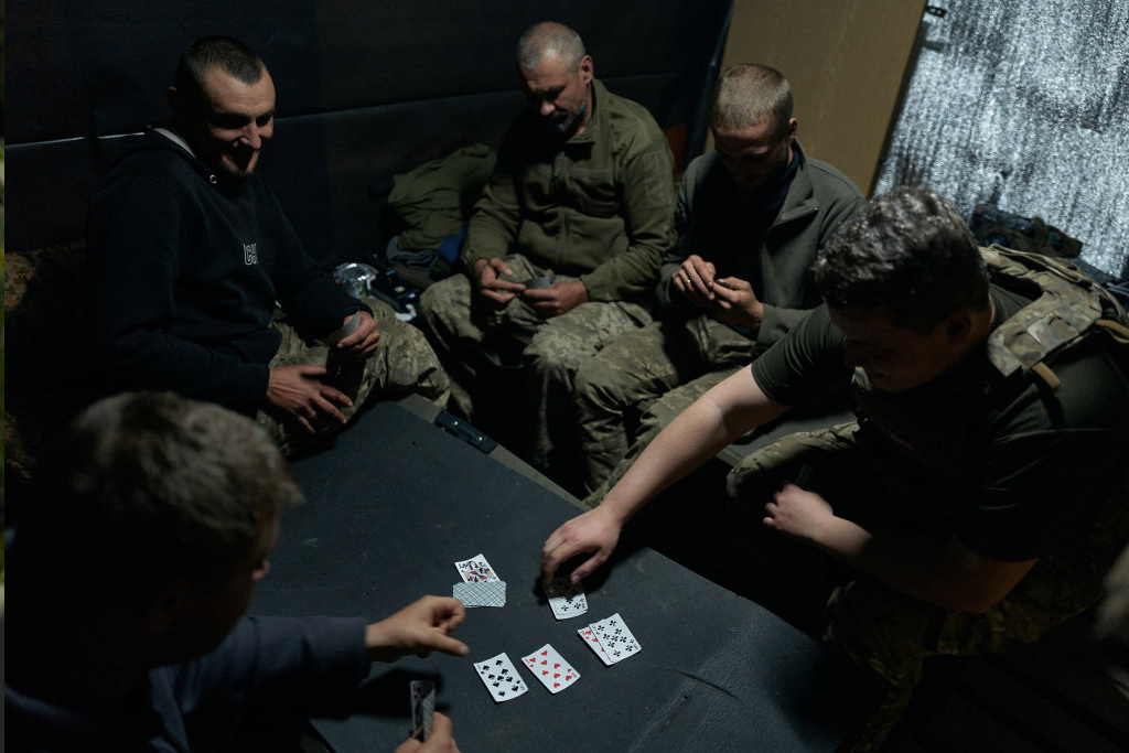 Ukrainalaiset sotilaat pelaavat korttia hämärässä huoneessa tai teltassa.