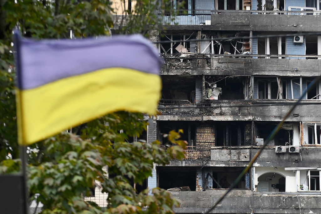 Ukrainan lippu liehuu vaurioituneen kerrostalon edessä Kiovassa lennokki-iskun jäljiltä.