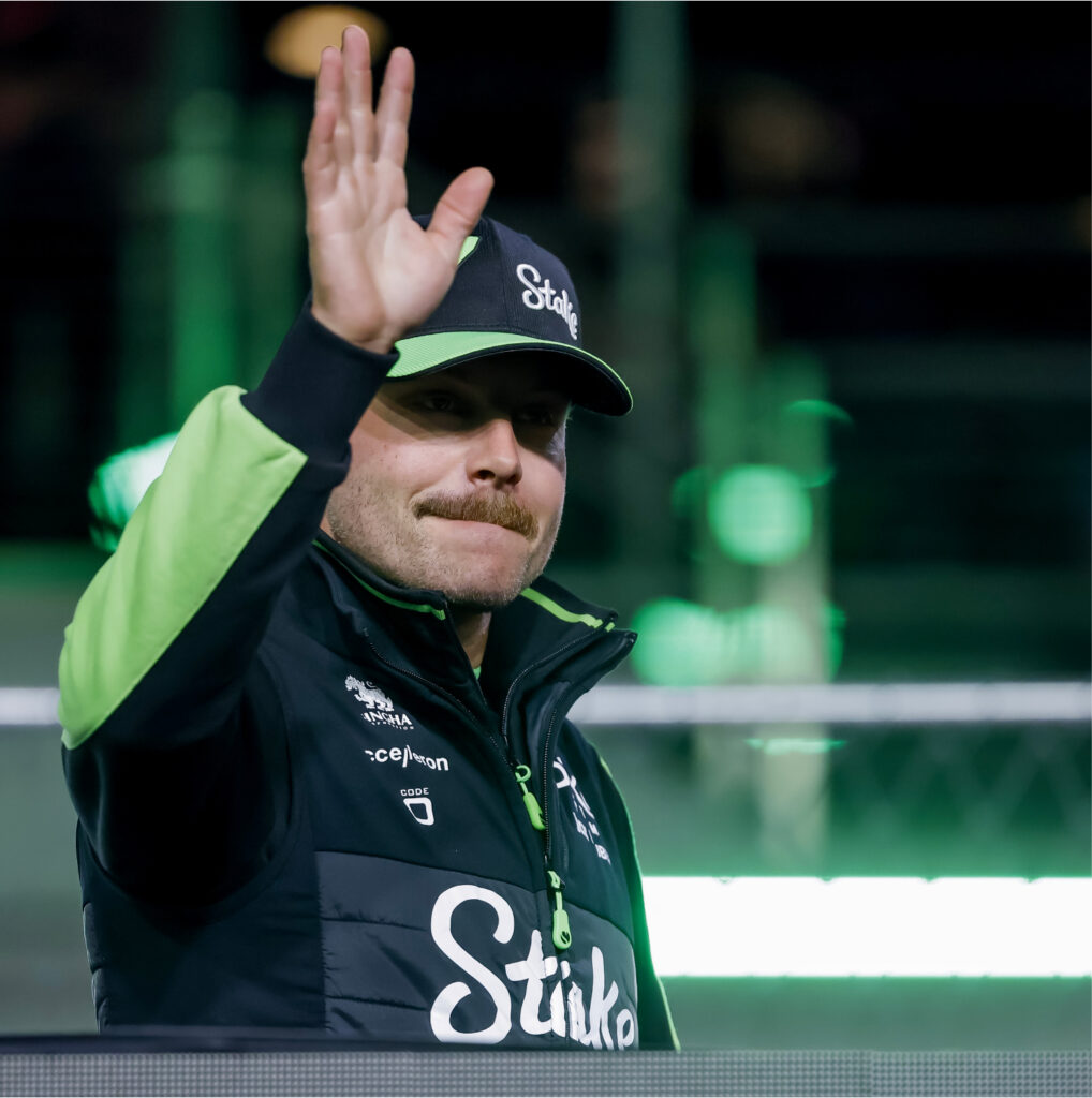 Valtteri Bottas vilkuttaa. Staken logo lippiksessä ja takissa.
