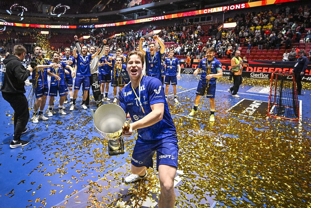 Suomen Justus Kainulainen juhlii pokaalin kanssa voiton jälkeen Ruotsin ja Suomen välisessä finaalissa miesten salibandy-maailmanmestaruuskisoissa 2024. Olkapäässä näkyy Veikkaus logo.