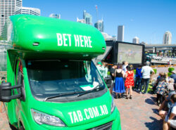 Tab-vedonlyöntiyhtiön auto mikä ilmoittaa että vedonlyönti on mahdollista täällä (autossa). Taustalla aurinkoinen Sydneyn kaupunkimaisema. Auto on parkkeerattu ravikisakatsomon eteen.