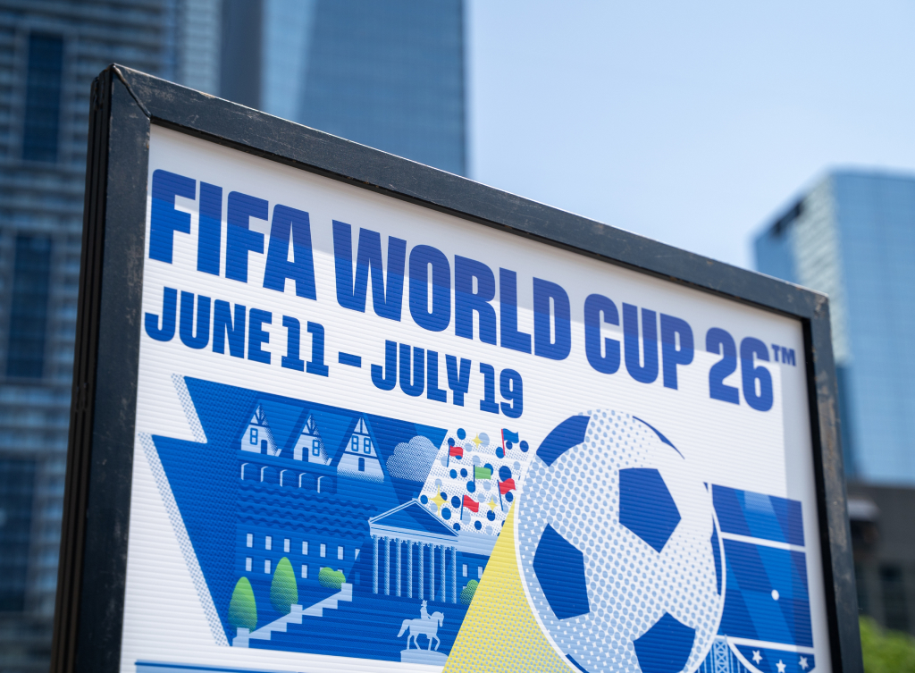 FIFA World Cup 2026 -mainosjuliste, jossa näkyvät päivämäärät June 11 – July 19 sekä jalkapalloteemainen grafiikka modernin kaupungin taustalla