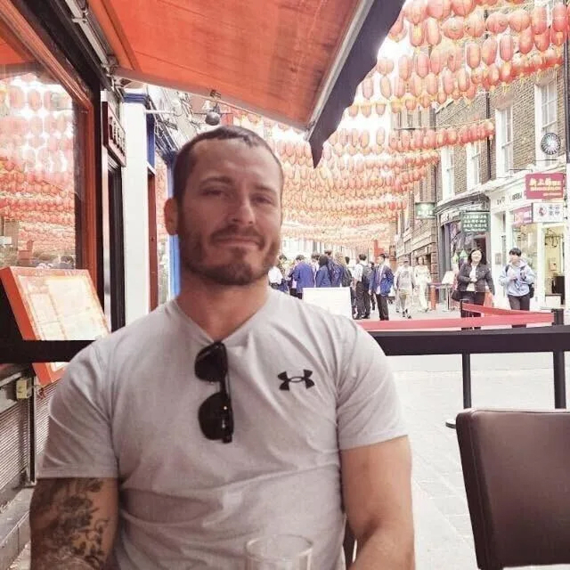 Mies istuu ravintolaterassin pöydän ääresä. Lihaksikas ja tyypillisen sotilaan näköinen henkilö.