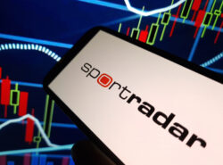 Sportradar logo auki puhelimella. Taustalla kurssikuvaaja.