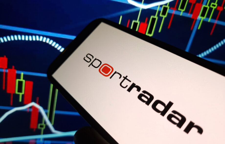 Sportradar logo auki puhelimella. Taustalla kurssikuvaaja.
