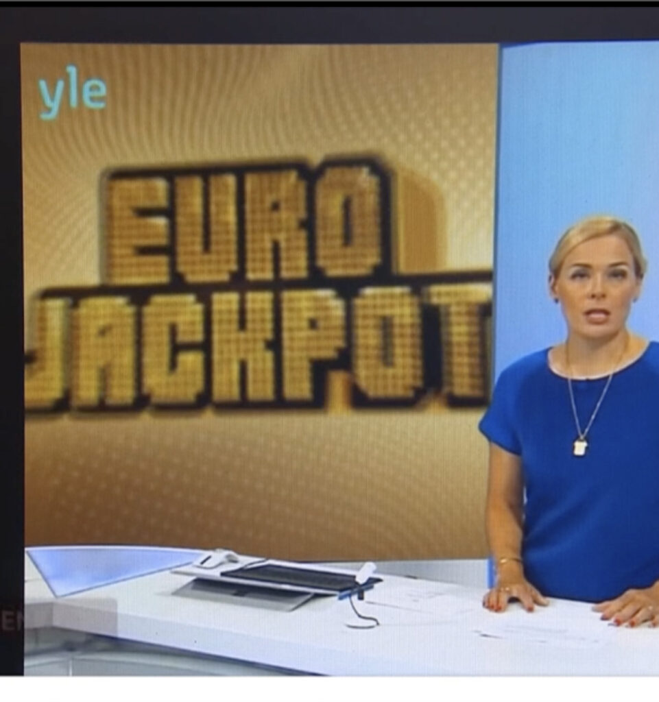 Ei-aidon-Ylen uutislähetys, jossa taustalla teksti Eurojackpot ja uutisankkuri studiossa, esimerkki rahapeliaiheisesta sisällöstä jota huijaukset voivat jäljitellä.