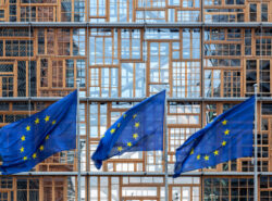 Euroopan unionin liput. Kolmen Euroopan unionin lipun sarja, jotka liehuvat tuulessa EU:n neuvoston rakennuksen julkisivun edessä Brysselissä. Europa-rakennuksen ulkoasu. Julkisivun kunnostetut ikkunapuitteet.