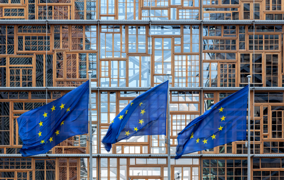 Euroopan unionin liput. Kolmen Euroopan unionin lipun sarja, jotka liehuvat tuulessa EU:n neuvoston rakennuksen julkisivun edessä Brysselissä. Europa-rakennuksen ulkoasu. Julkisivun kunnostetut ikkunapuitteet.