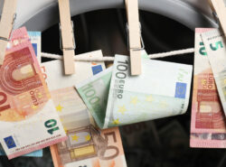 Rahanpesua kuvaava kuva. Euroja pyykkinarulla, taustalla pesukone.