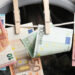 Rahanpesua kuvaava kuva. Euroja pyykkinarulla, taustalla pesukone.