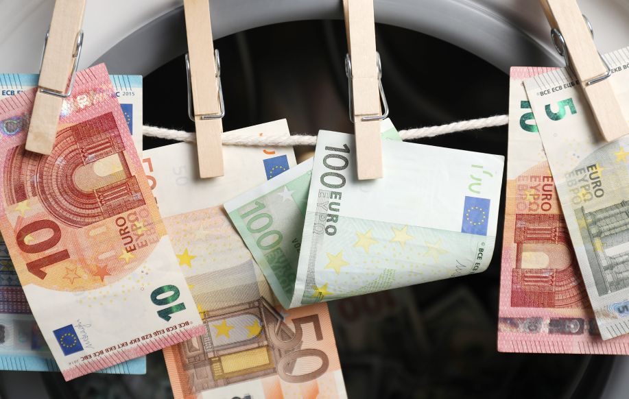 Rahanpesua kuvaava kuva. Euroja pyykkinarulla, taustalla pesukone.