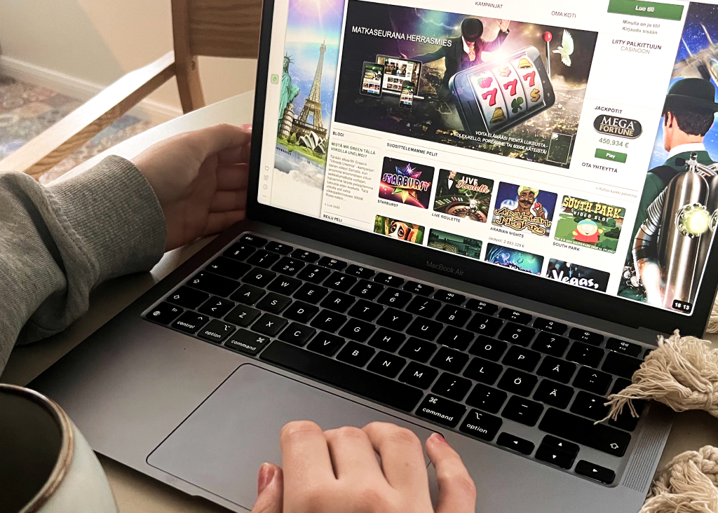 Nainen selaa nykyaikaisella Macbook Air tietokoneella retron näköistä Mr Green nettikasinoa. Peleinä näkyy esimerkiksi Starburst, Arabian Nights ja Mega Fortune.