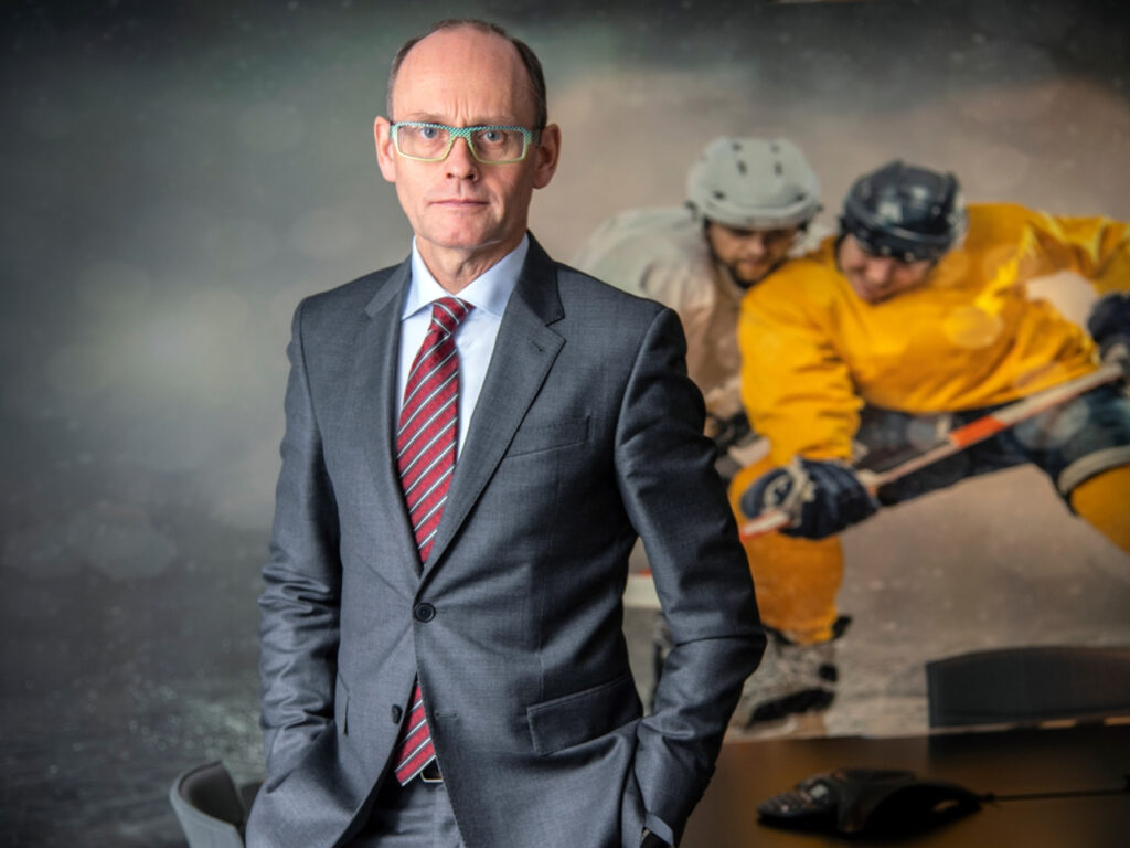 Pontus Lindwall tyylikkäässä puvussa kädet taskussa. Taustalla lätkänpeluuta miehekkäässä tunnelmassa.