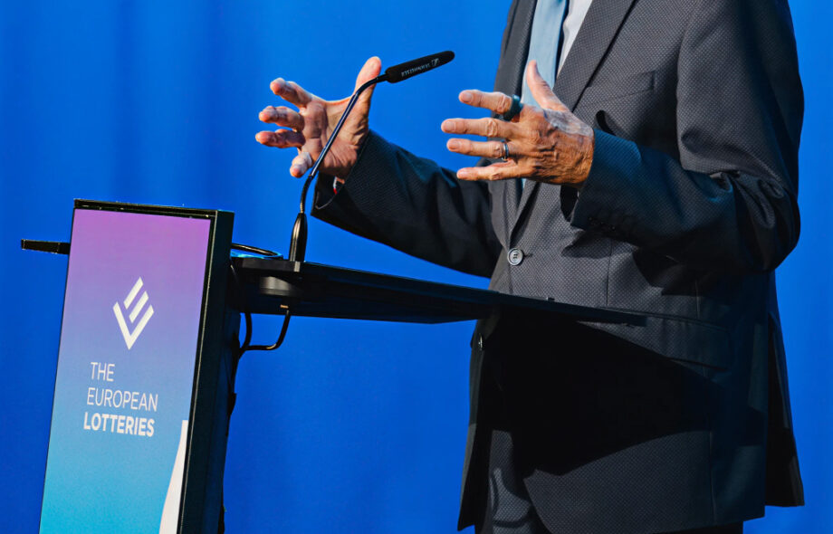 Mies heiluttelee käsiään modernissa puhujanpöntössä missä merkattuna "European Lotteries"