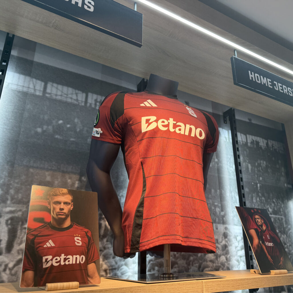 Urheilukaupassa AC Sparta Praha pelipaita näytillä. Vieressä kuvia pelaajista paita päällä. Suuri Betano logo.