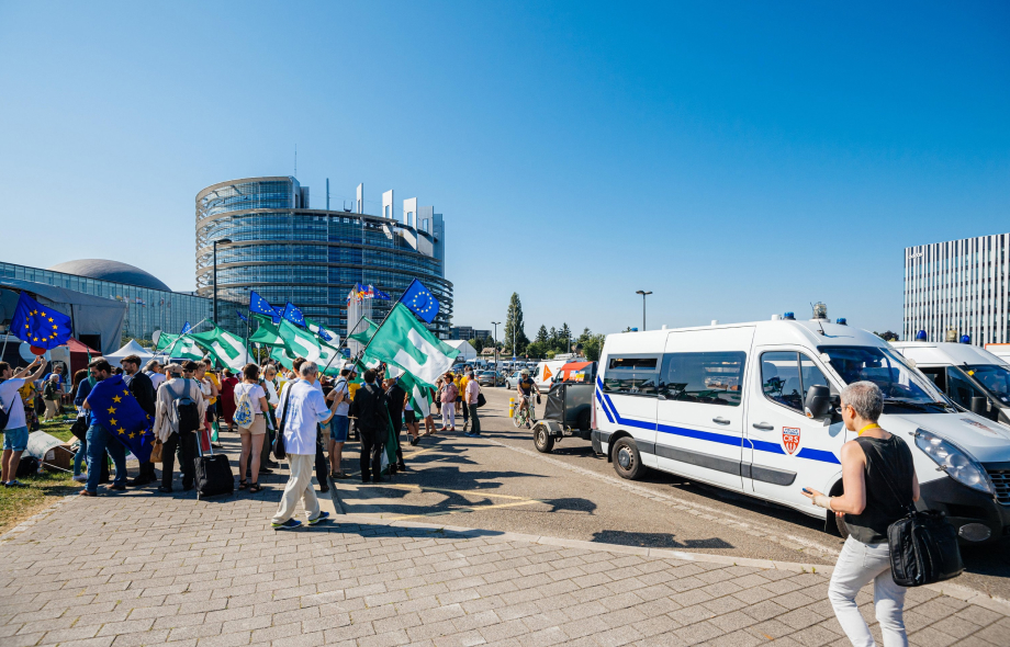 Ihmisiä EU ja Federalistilippujen kanssa Louise Weiss parlamenttirakennuksen edessä. Vieressä poliisiautoja.
