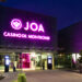 JOA Casino De Montond sisäänkäynti. Moderni tyyli, muutama kasvi näkyy. Liilat ledivalot nimikyltissä.