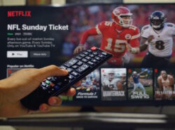 Television ruudulla näkyy Netflixin urheilusisältöä ja NFL-aiheinen ohjelmavalikko, kun katsoja pitää kaukosäädintä kädessään.