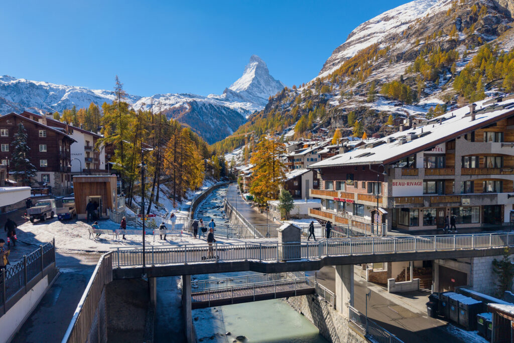 Sveitsiläisen kaupungin/kylän läpi kulkee virta. Silalla sähköskuutti. Taustalla Matternhorn.